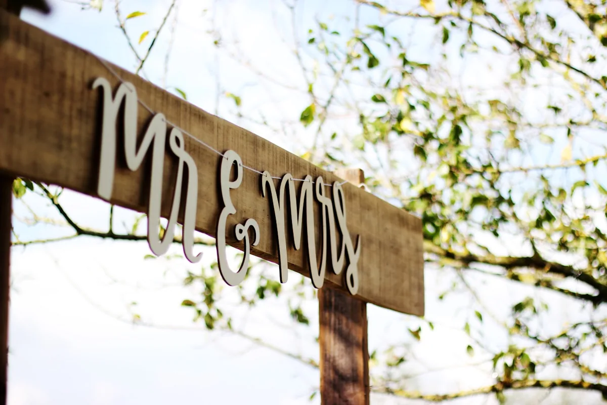 Hand-lettered wedding sign among leafy outdoor branches